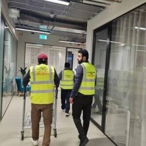 Workers in high-visibility vests moving through an office corridor with a trolley – representing professional office relocation services