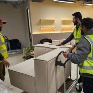 Movers in high-visibility vests transporting a sofa on a trolley during an indoor relocation.