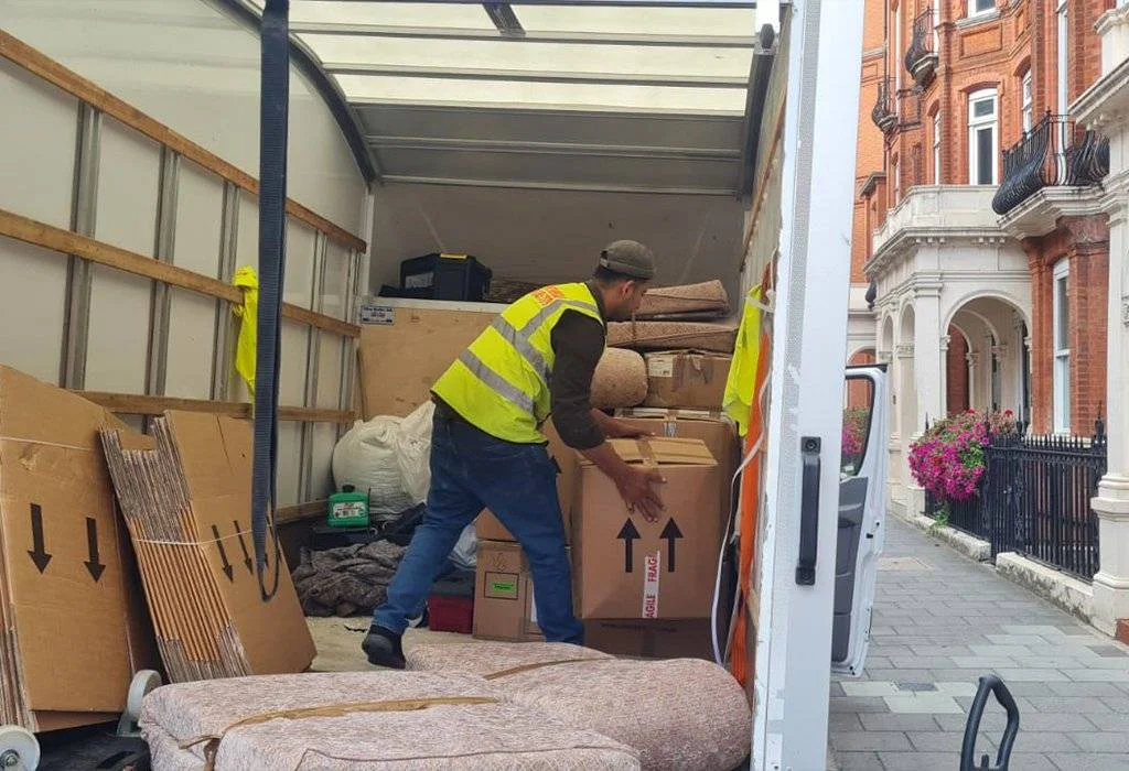 A man wearing 247 Moving Company west arranging boxes in the van.