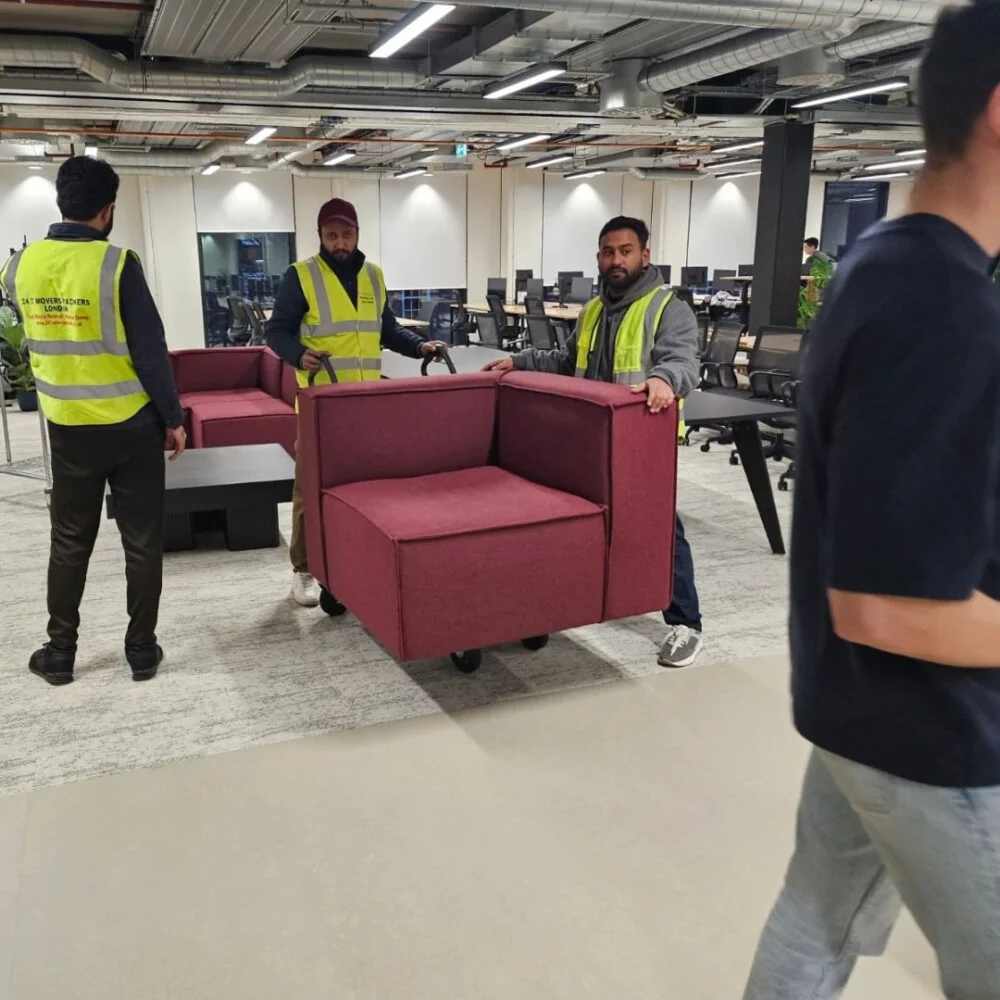 Professional movers from 24/7 Movers Packers London carefully carrying a maroon sofa section during an office relocation service.
