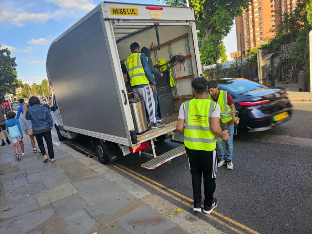 Movers from 24/7 Movers Packers London handling furniture and boxes at the back of a moving van parked on a busy London street.